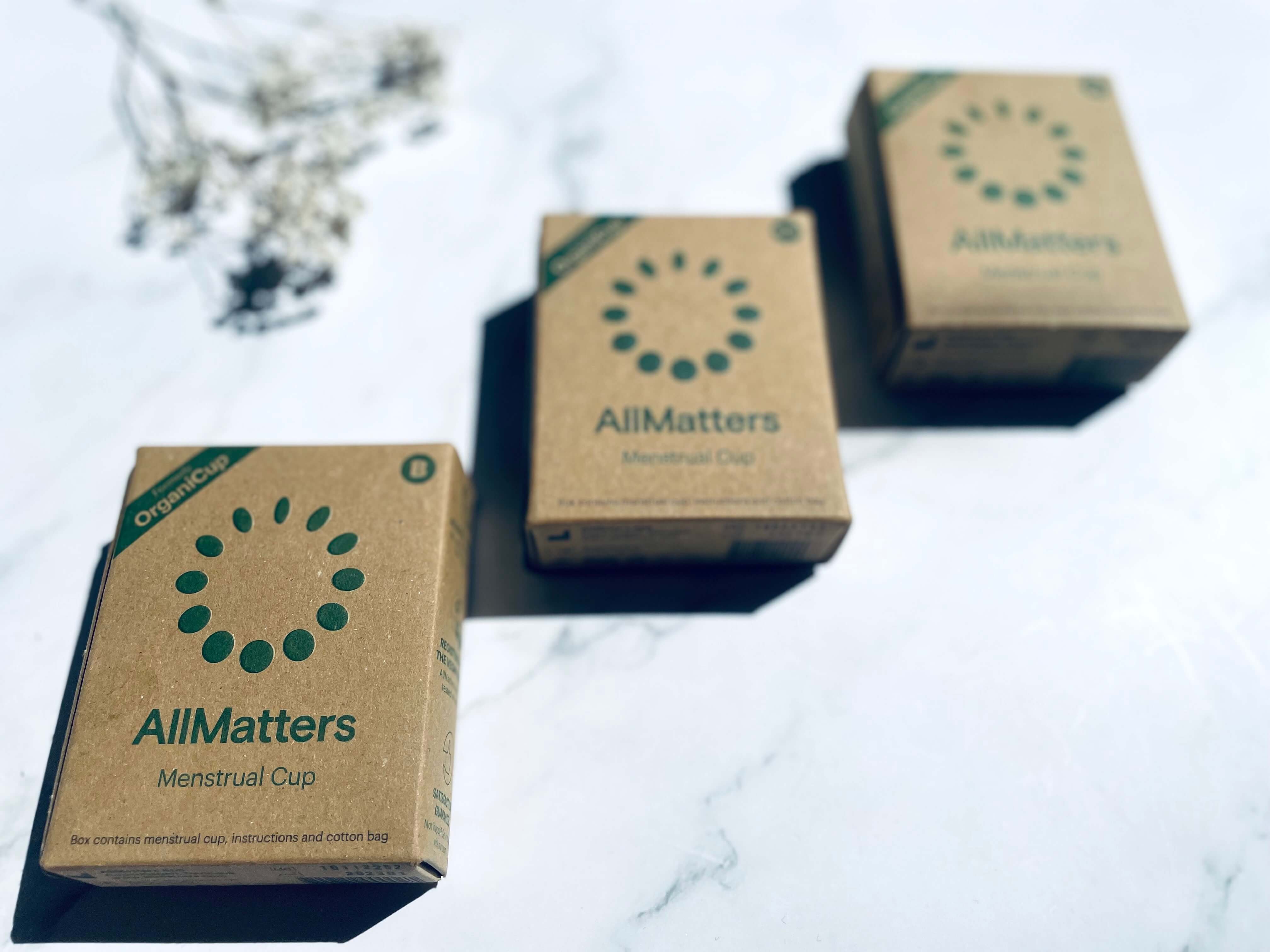 3 AllMatters menstruationskopper på et bord i deres indpakning