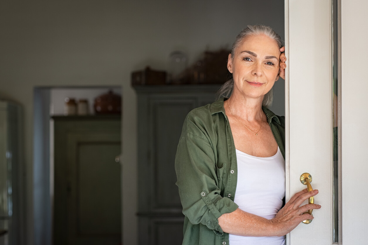 Ældre kvinde med gråt hår står i døråbning
