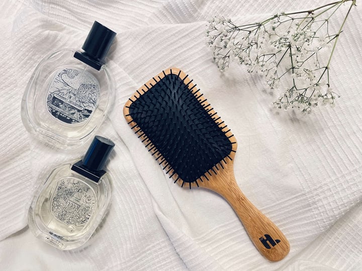 Hairlust Bamboo pladebørste på en seng med parfume
