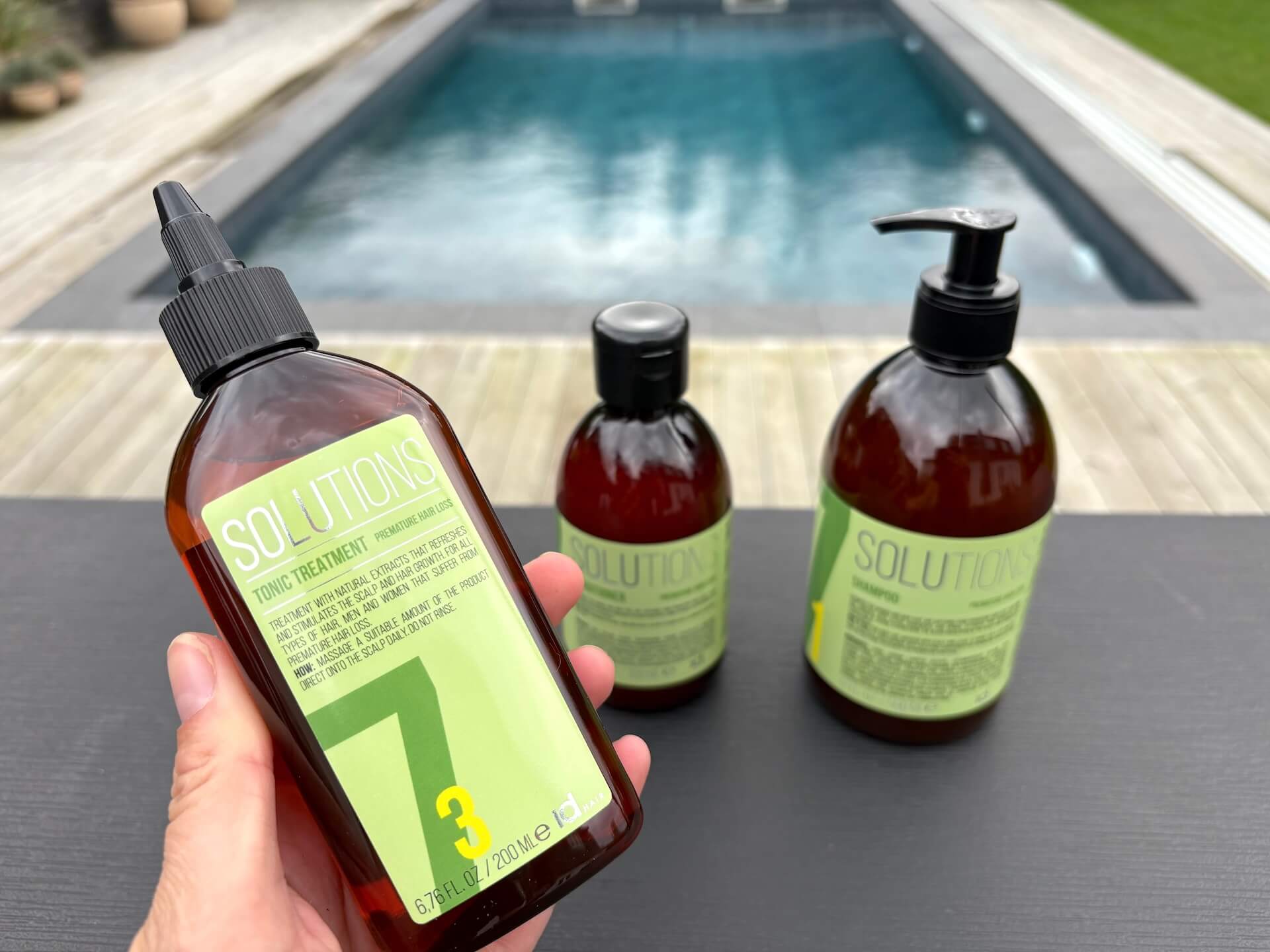 IdHAIR Solutions No.7-3 Tonic Treatment i hånd med shampoo og conditioner på bord bagved