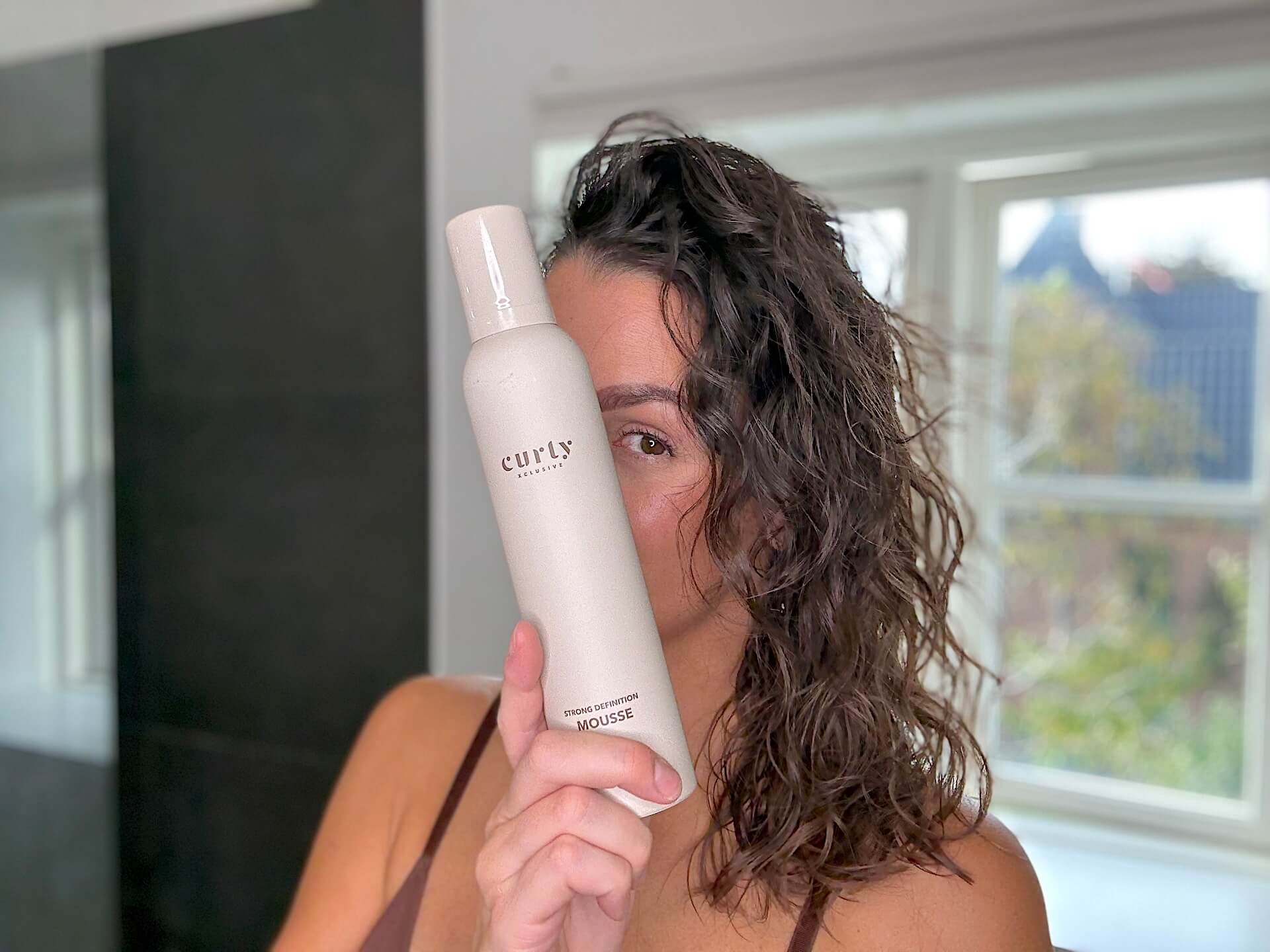 Kvinde der står med IdHAIR Curly Xclusive Strong Definition Mousse