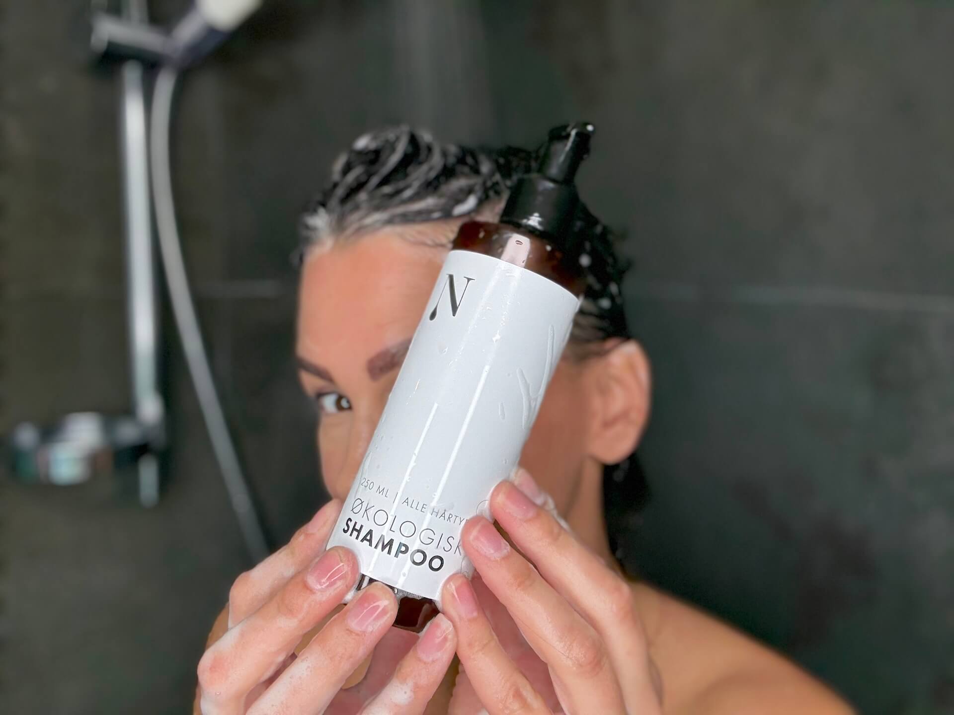 Kvinde der står med Naturligolie Shampoo i brusebadet