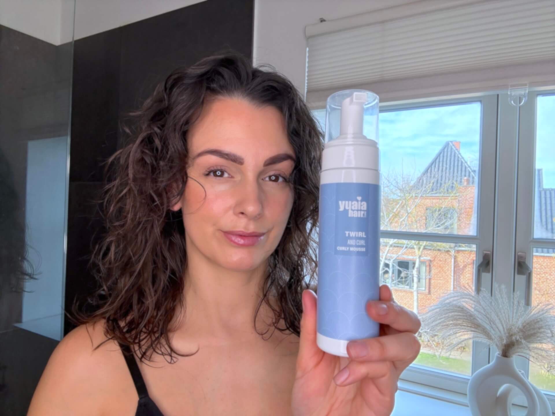 Kvinde der står med Yuaia Haircare Twirl and Curl Curly Mousse