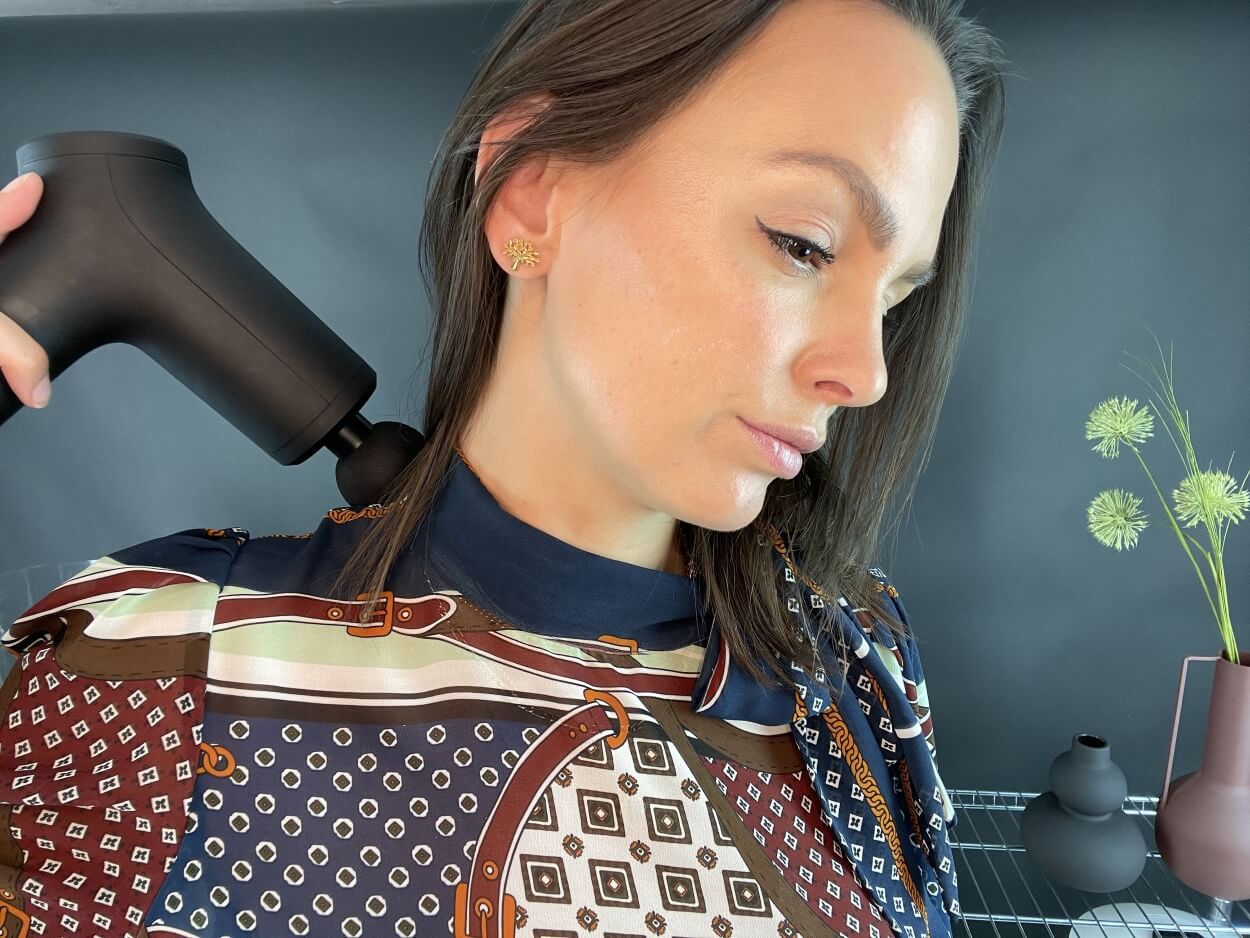 Kvinde masserer nakken med massagepistol