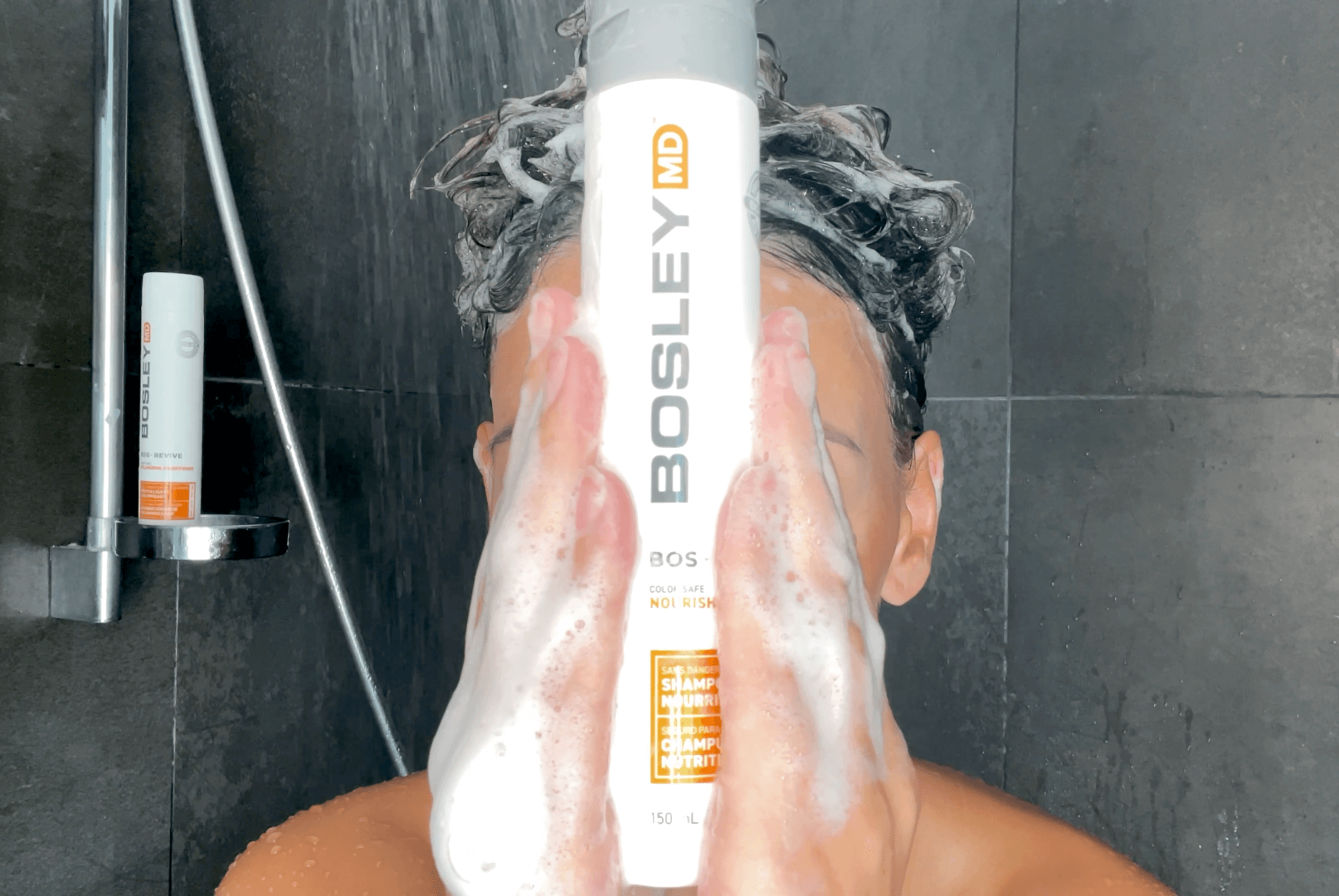 Kvinde med BosleyMD foran sit ansigt og shampooen i håret