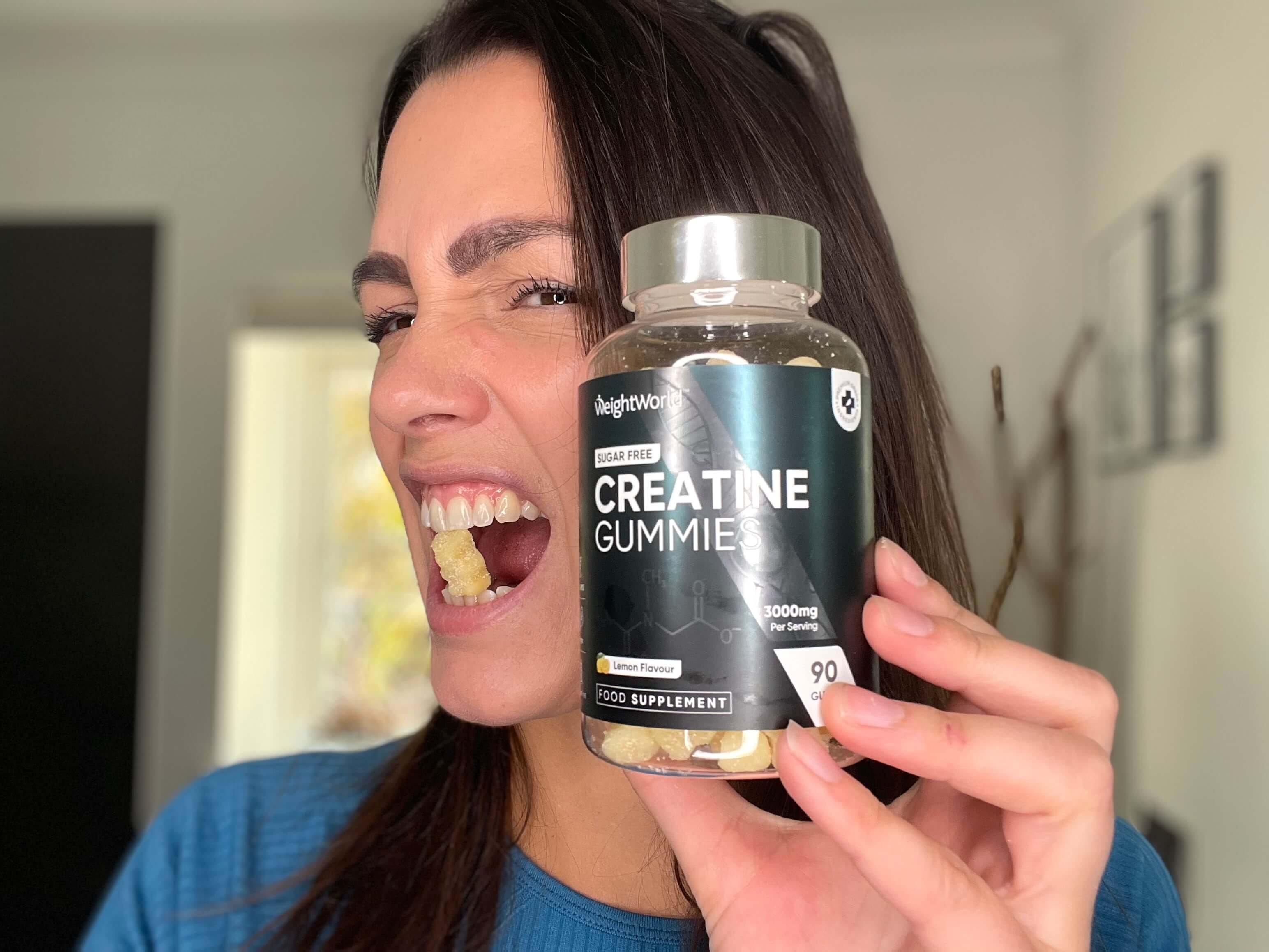 Kvinde med en vingummi i munden og Weightworld Creatine Gummies i hånden
