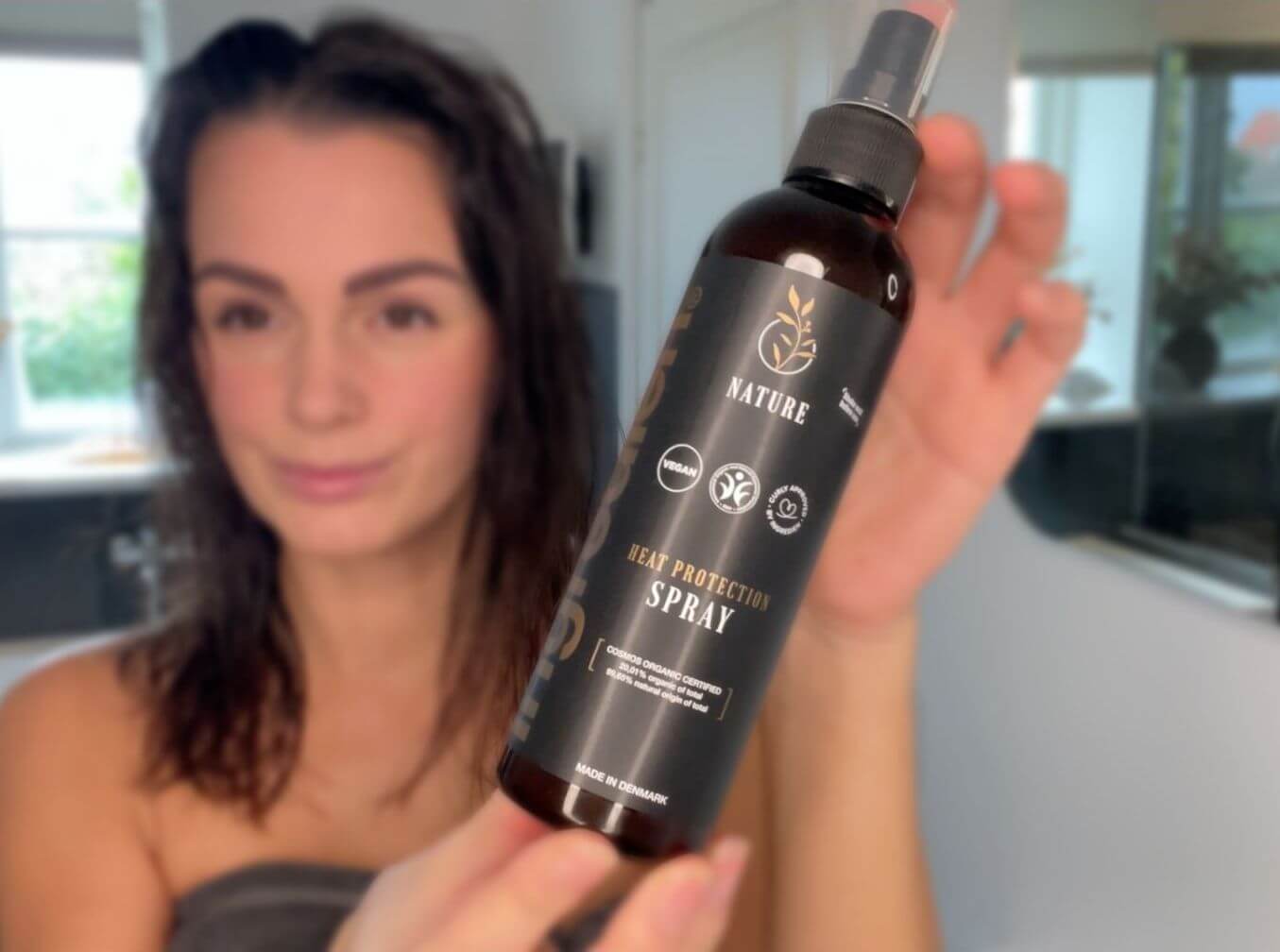 Kvinde med håndklædetørt hår med ingredien Nature Heat Protection Spray i hånden