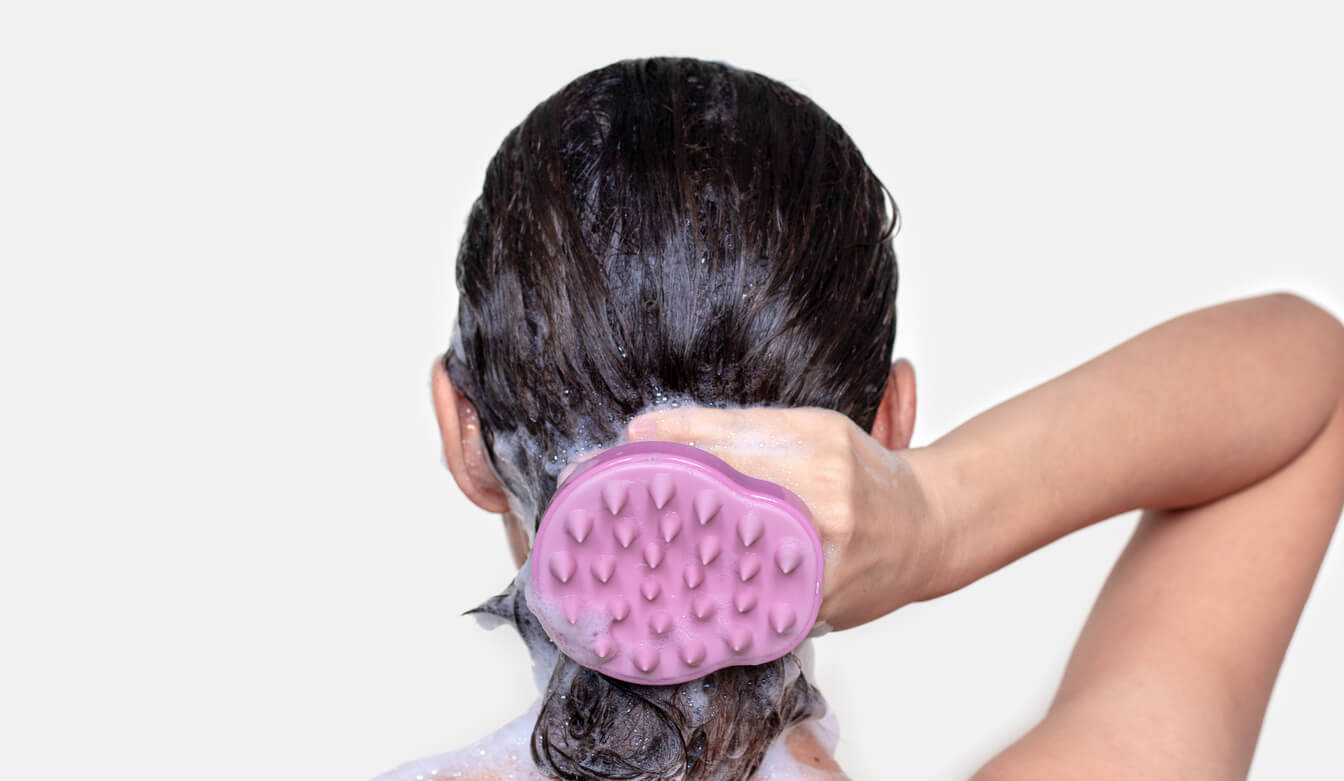 Kvinde med hovedbundsbørste brugt i vådt hår med skummende shampoo