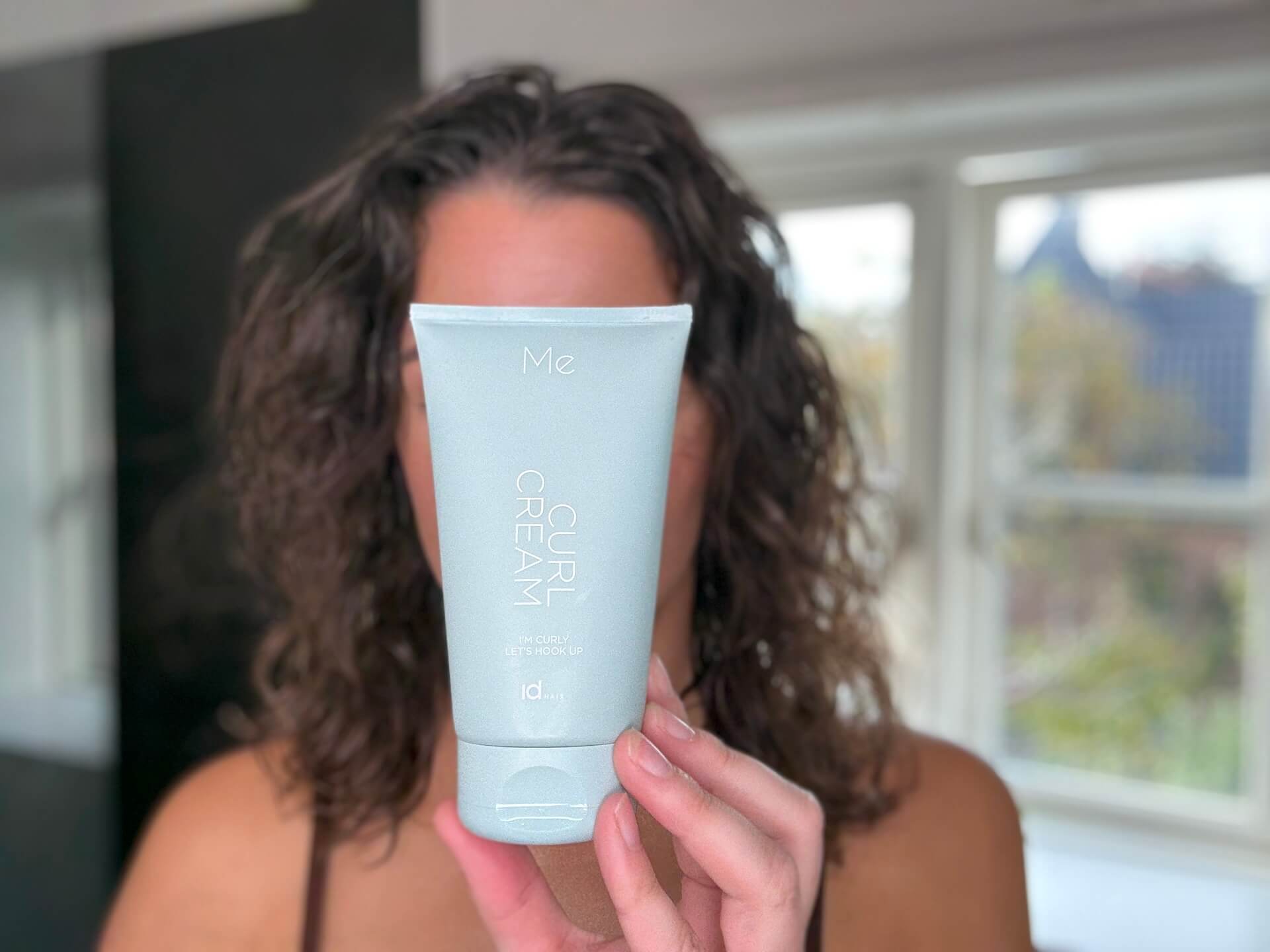 Kvinde med krøllet hår der står med IdHAIR Me Curl Cream