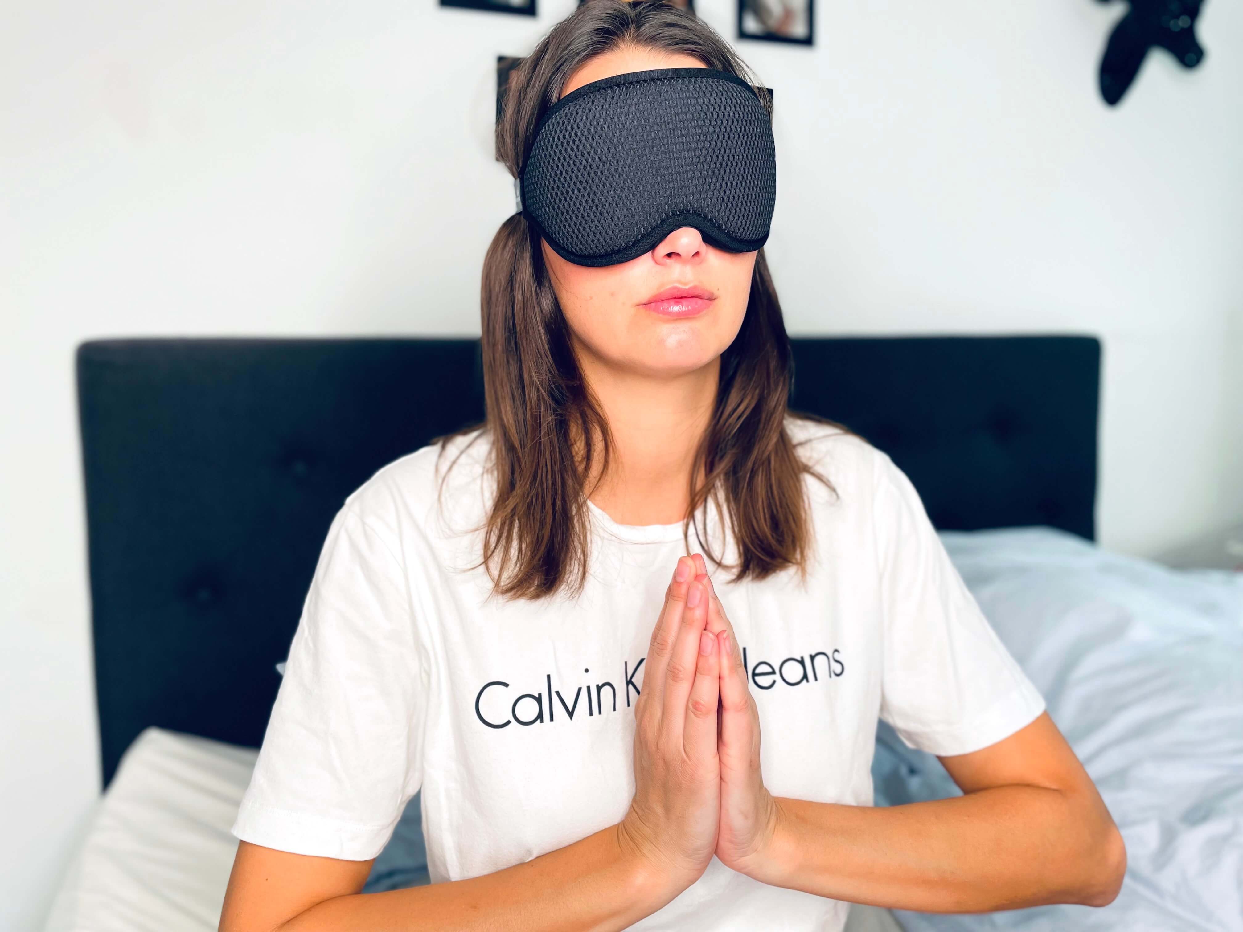 Kvinde med sovemaske mediterer i sengen