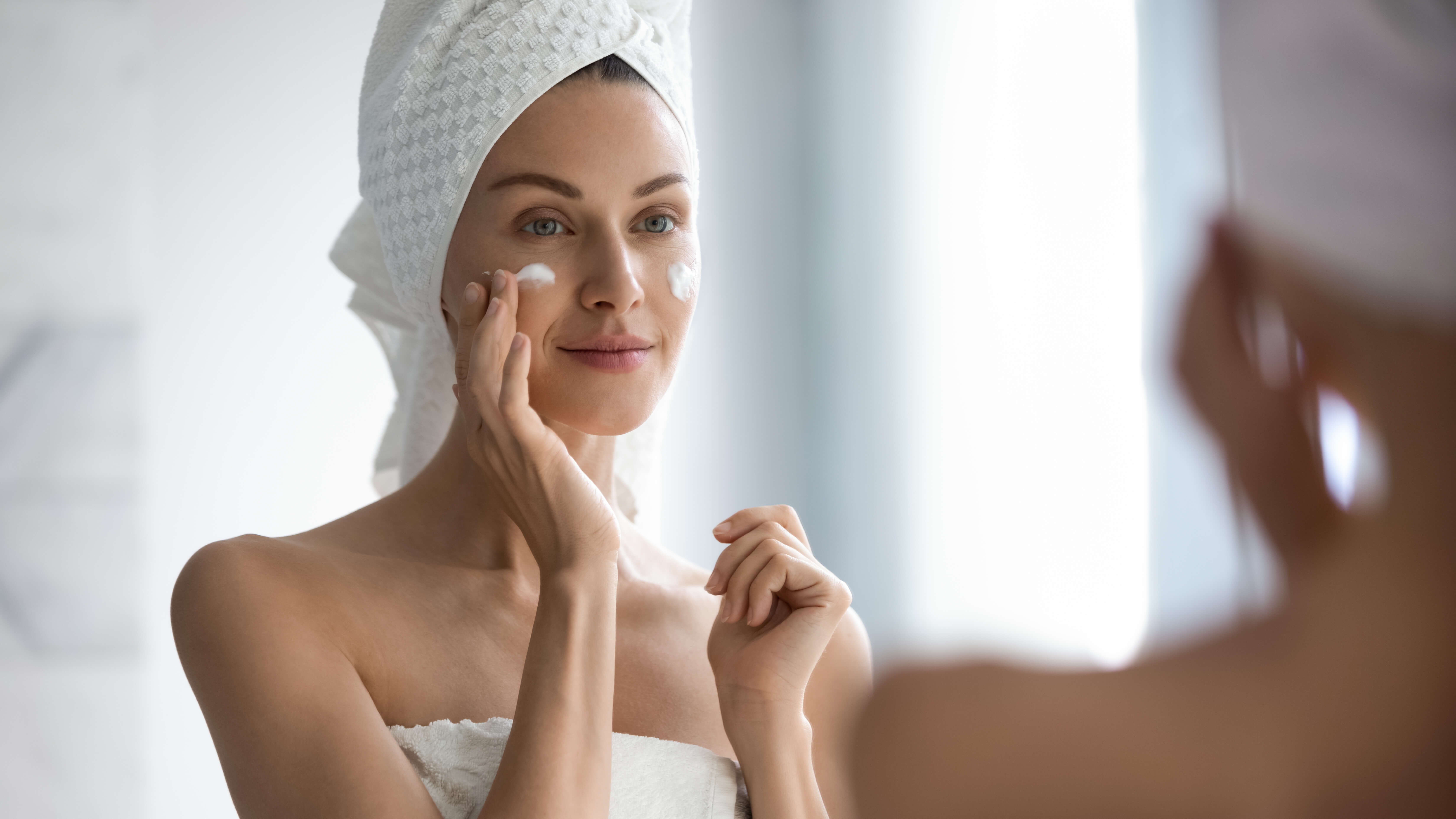 Kvinde smører retinol creme i ansigtet foran spejl i badeværelse