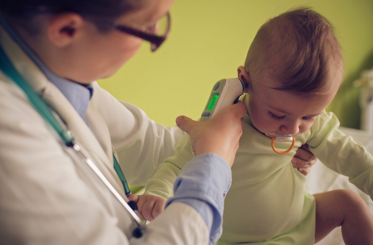 Læge måler temperatur med øretermometer i øre på baby