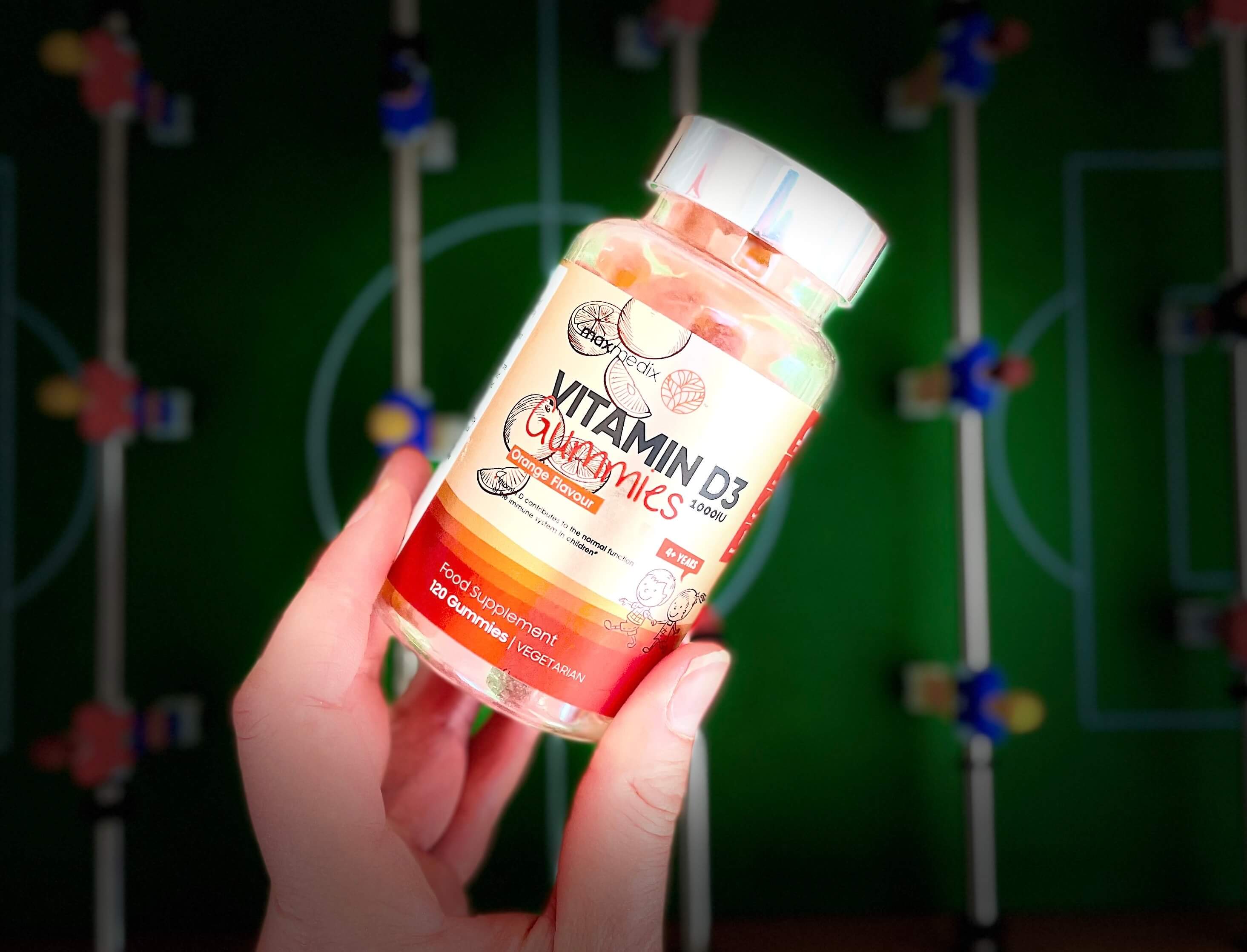 MaxMedix D3-vitamin Gummies i hånd over fodboldbord