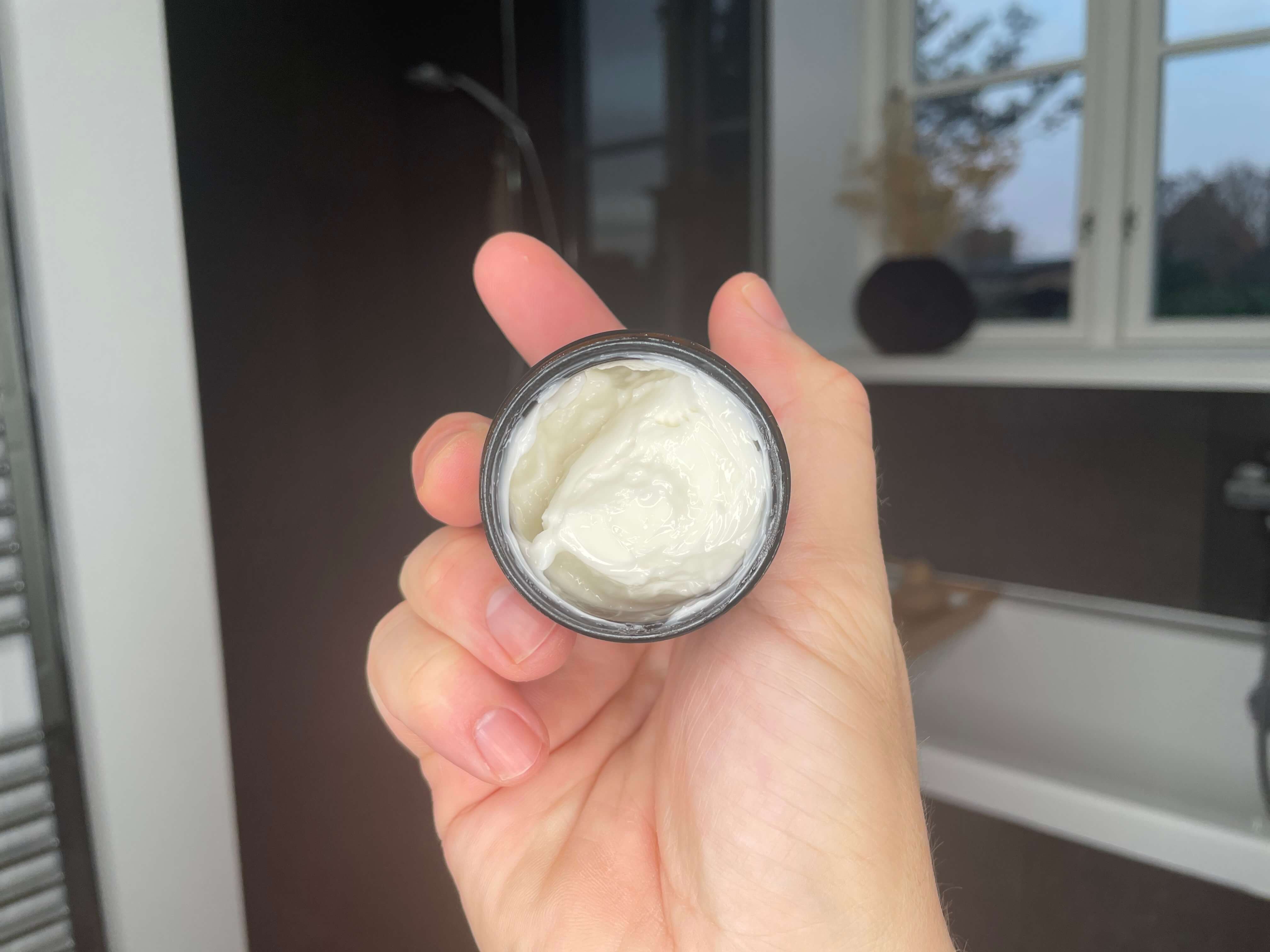 Pomp & Co Beard Balm der er åben i en hånd på et badeværelse