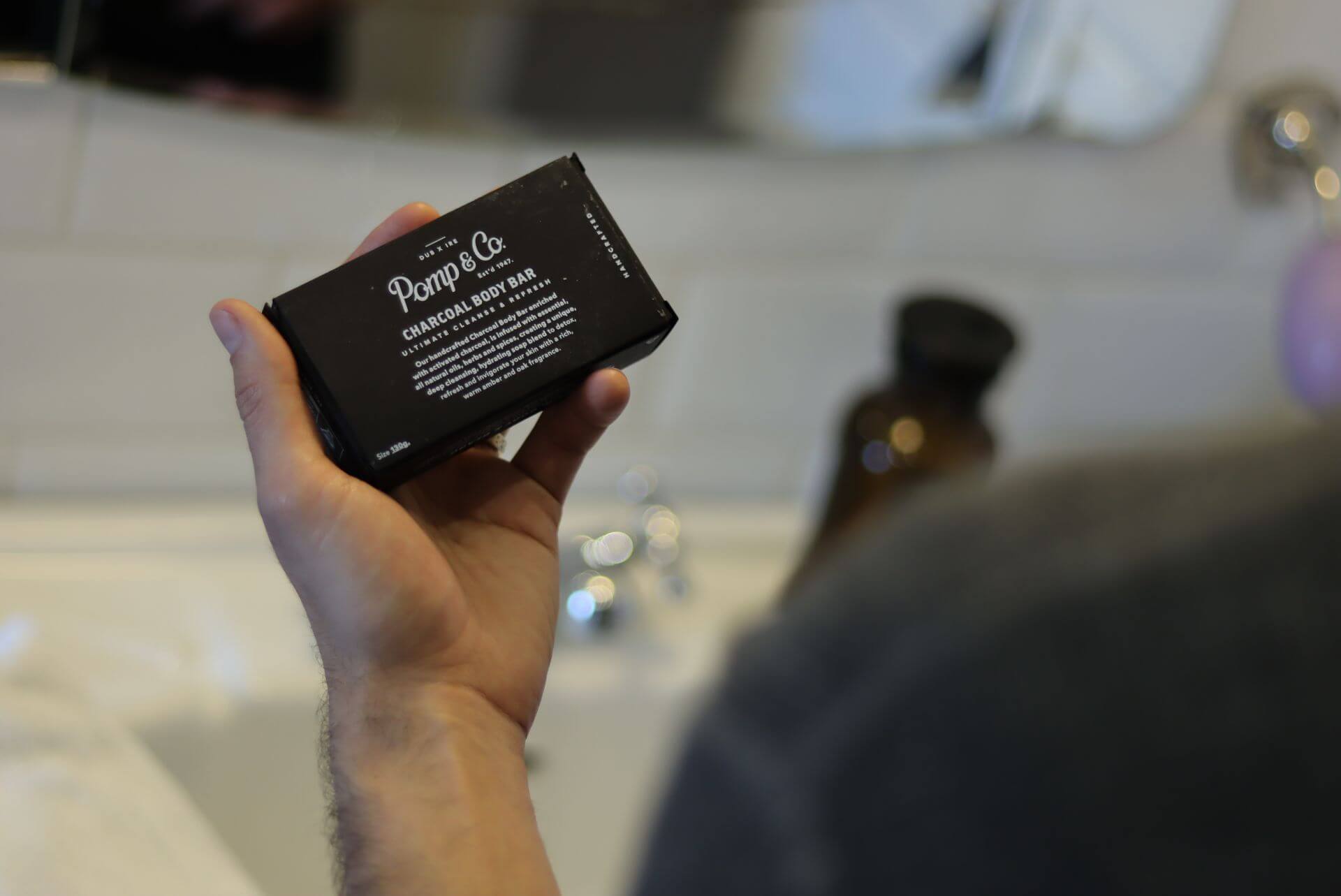 pomp & co charcoal sæbebar i hånden på en mand på et badeværelse