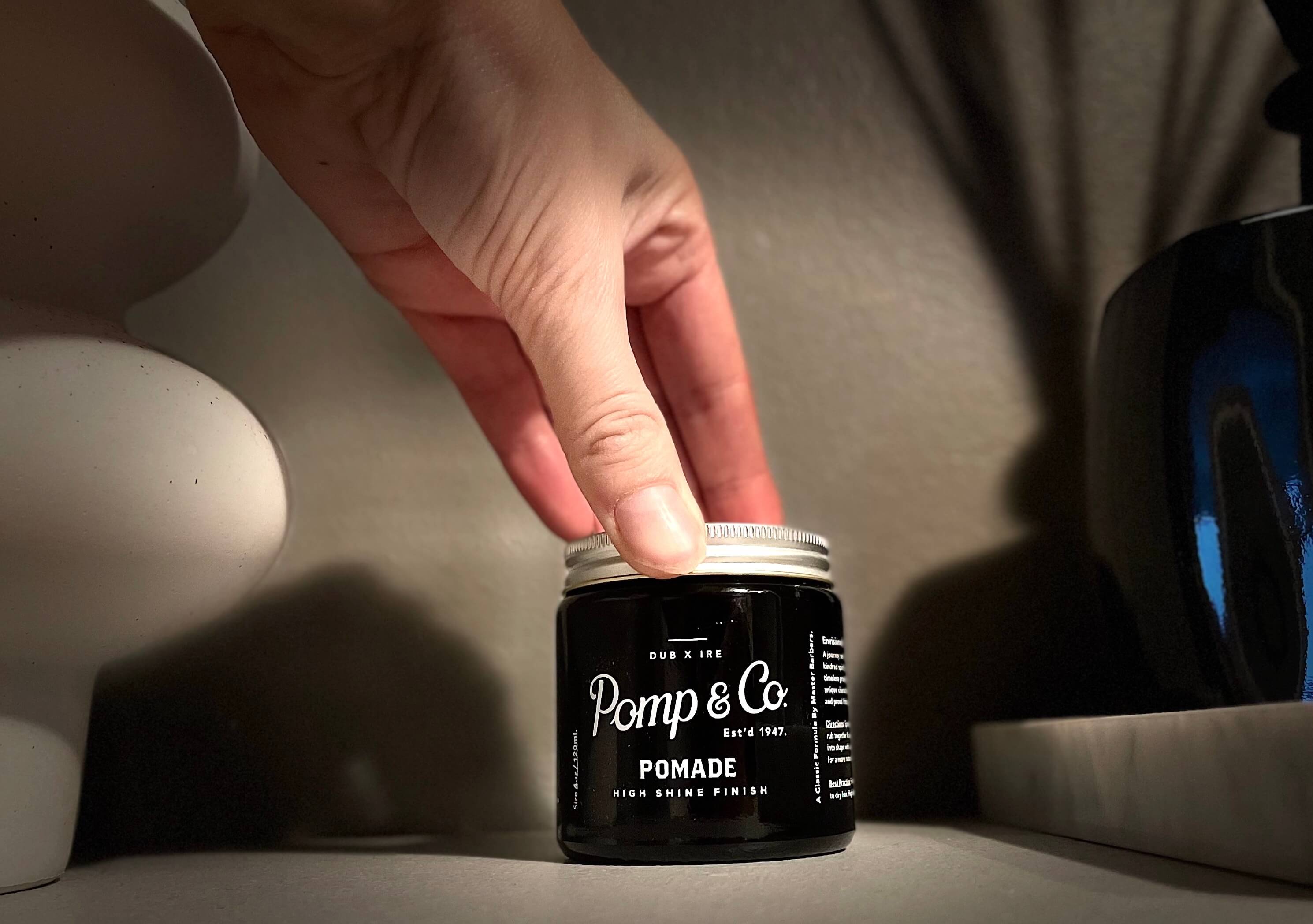 Pomp & Co pomade på et badeværelse med en hånd ovenpå