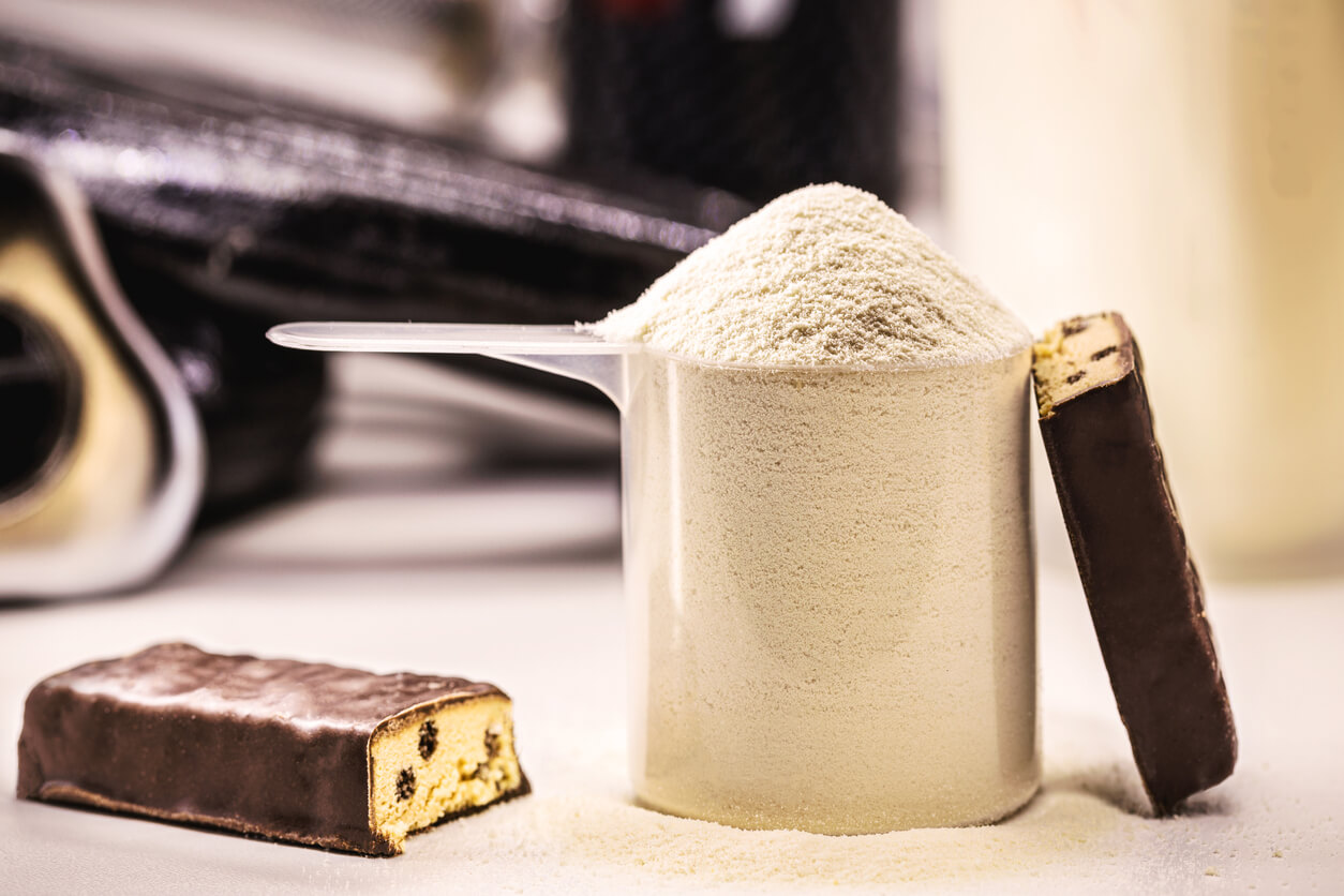 Proteinpulver i scoop og knækket proteinbar på bord
