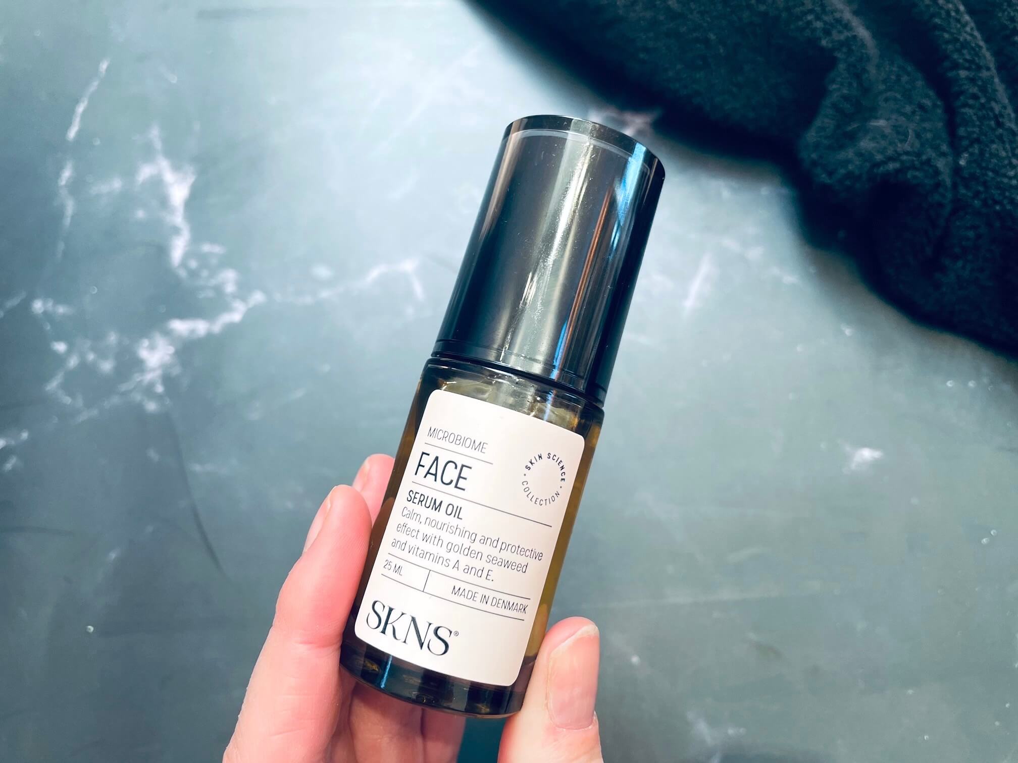SKNS Face Serum Oil i hånd med mørk baggrund