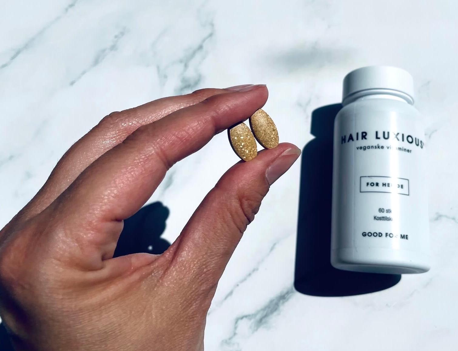 Tabletter som hårvitaminer til kvinder i mellem fingrene på kvinde