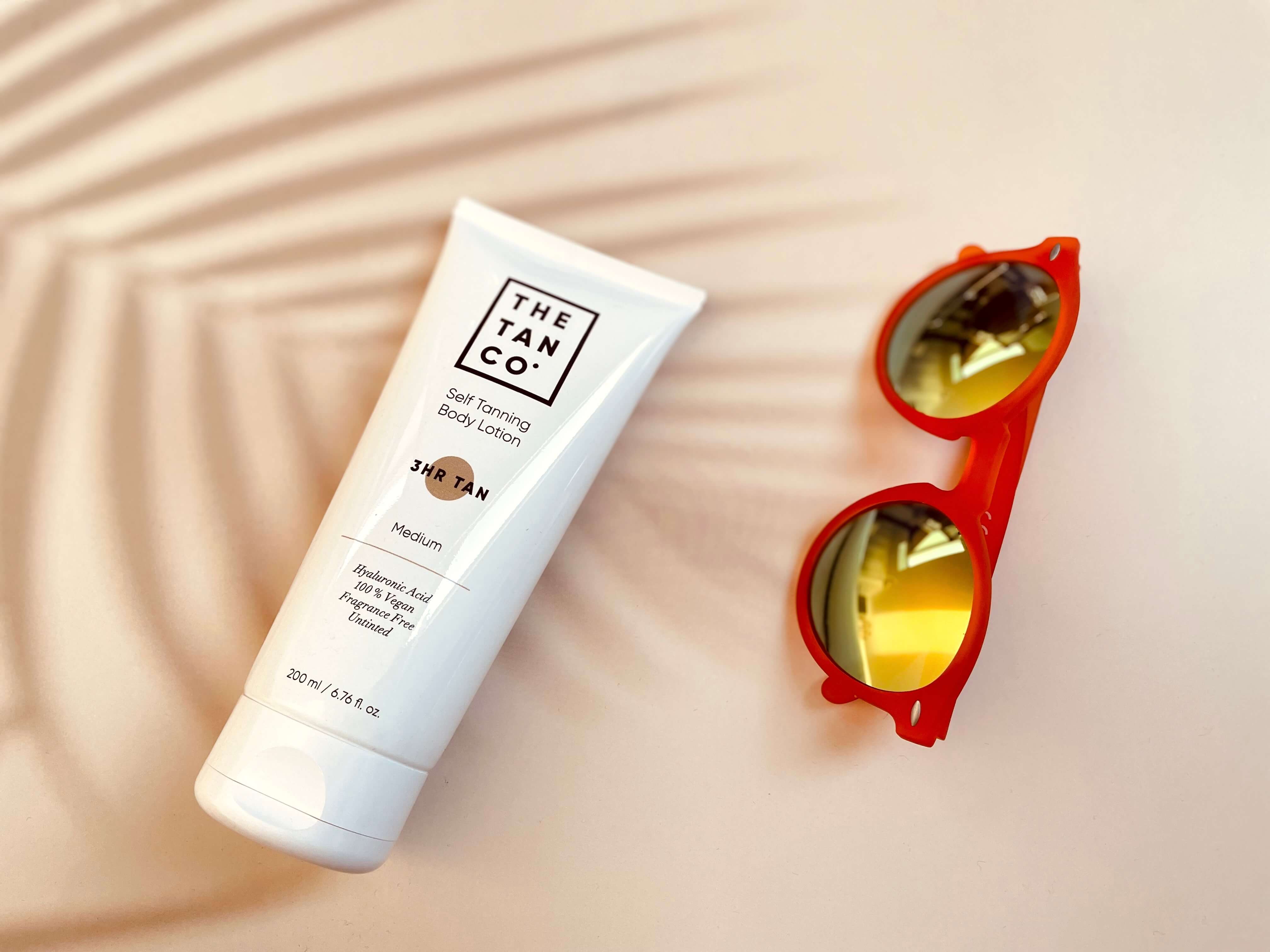 The Tan Co Self tanning bodylotion på bord med solbriller