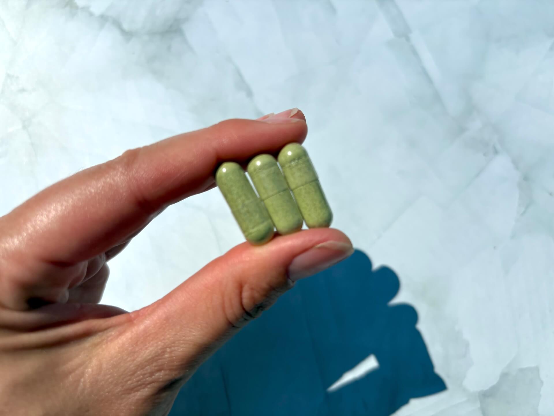 Tre kapsler Healthwell Moringa Kapsler ØKO imellem fingre