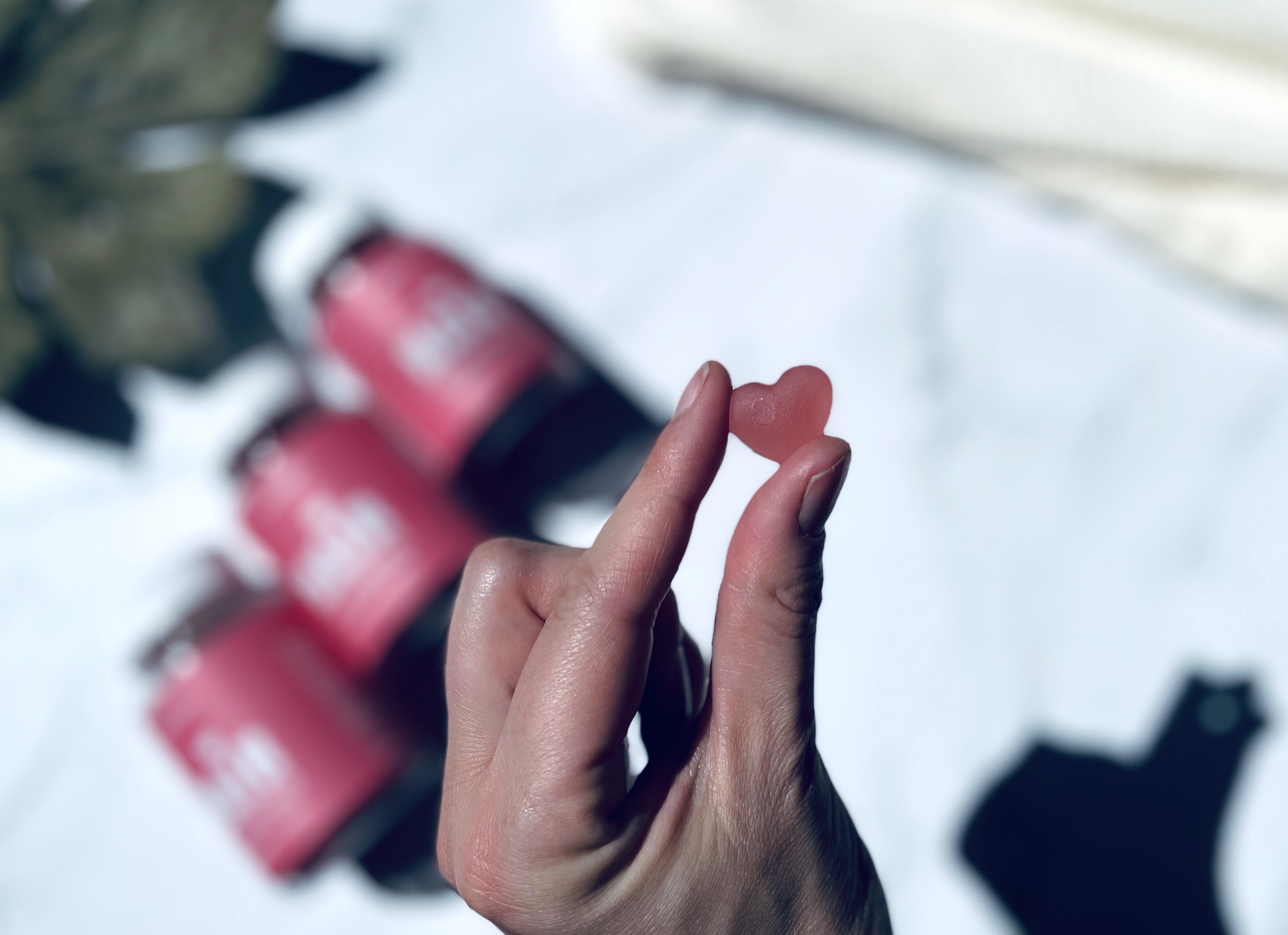 Yuaia Haircare Gummi Hair Vitamins i bøtter i baggrunden og i mellem to fingre